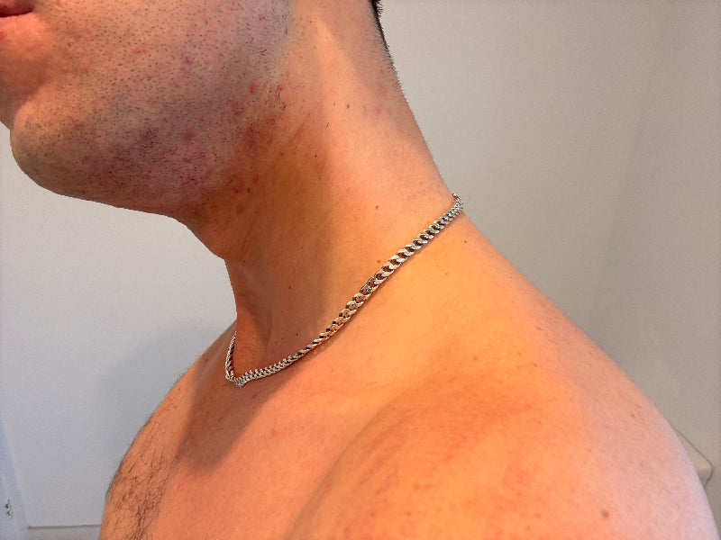 Close-up of a person wearing a silver chain necklace against a plain background